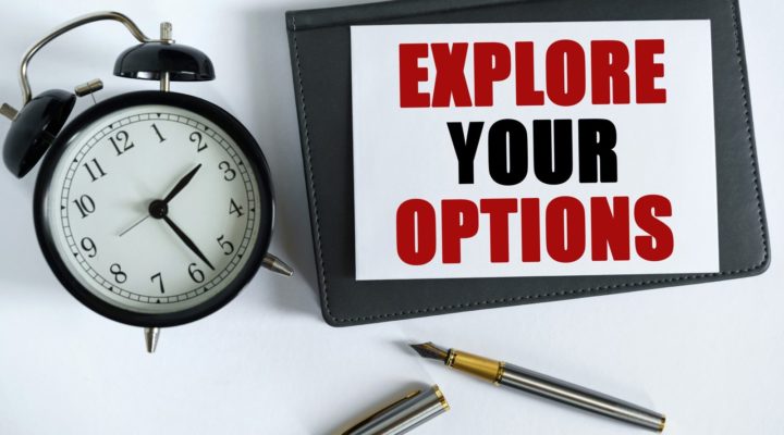 Desk with alarm clock, pen and iPad showing text "Explore your options"