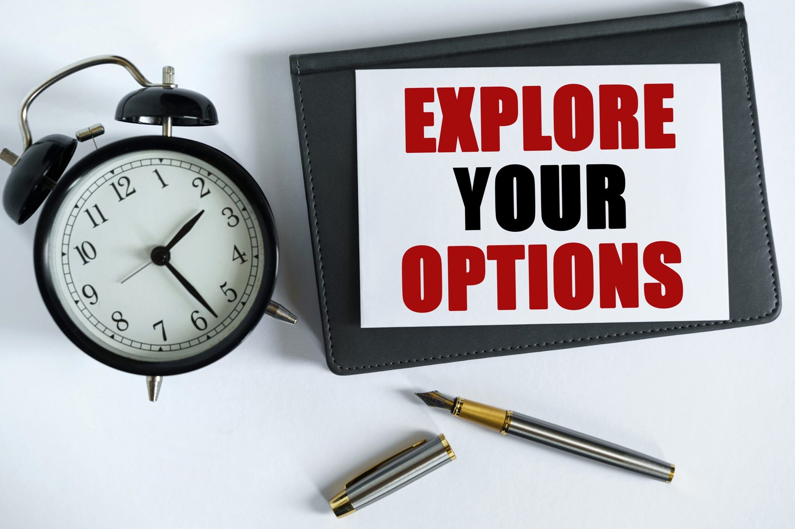 Desk with alarm clock, pen and iPad showing text "Explore your options"