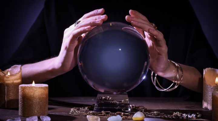 hands over a crystal ball with tarot cards on a table